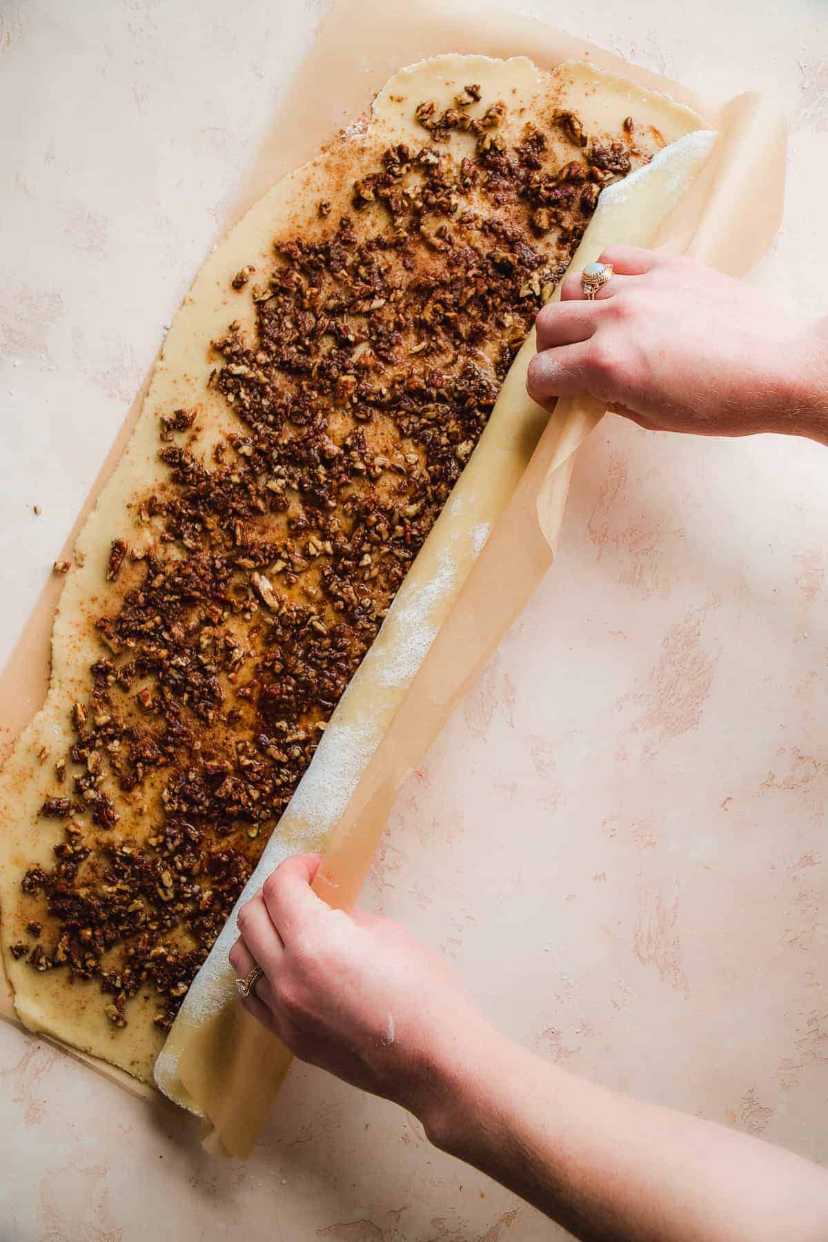 Person rolling up dough into cinnamon rolls.