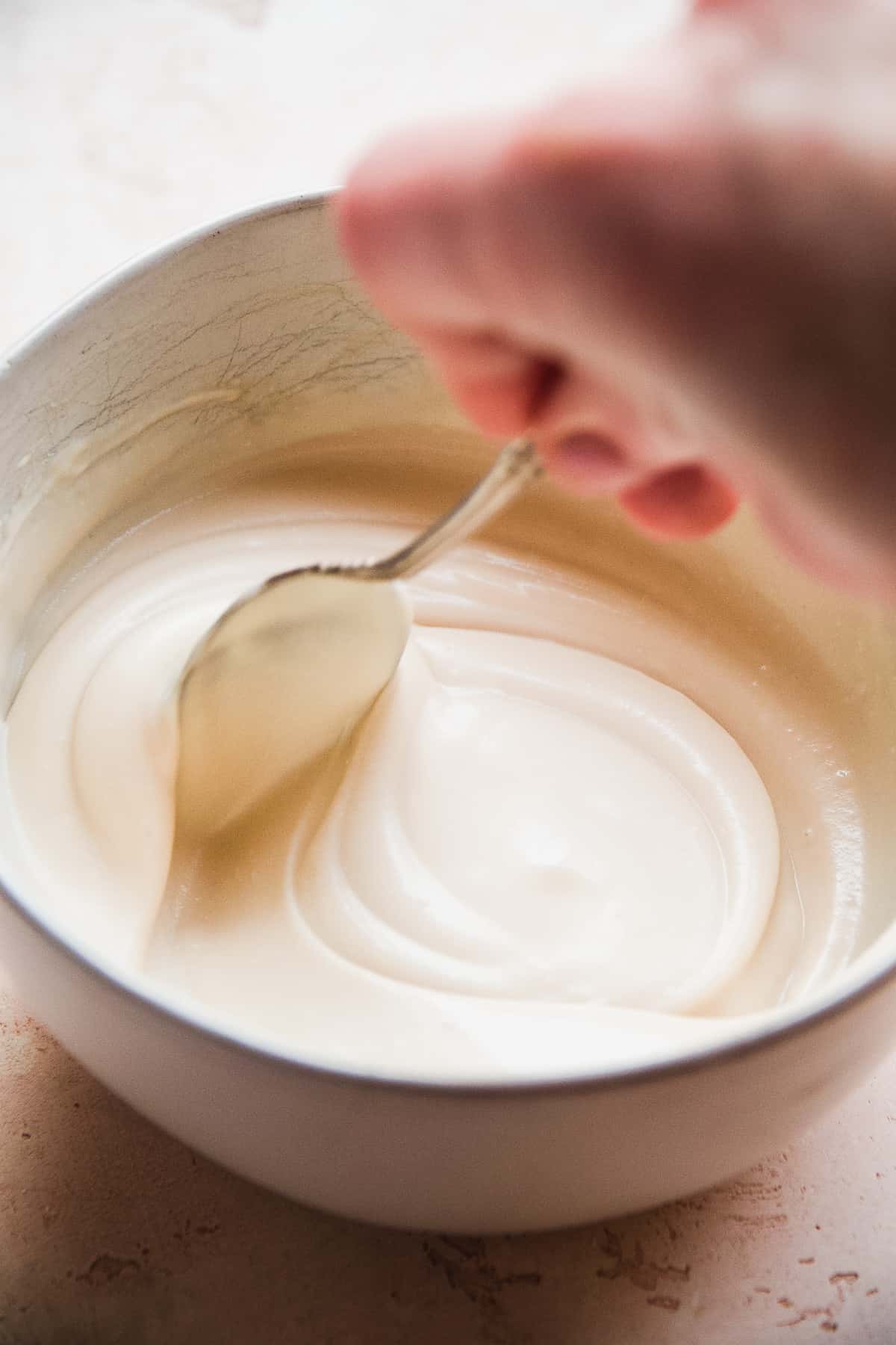 Hand swirling a spoon to mix cream cheese icing in an bowl.