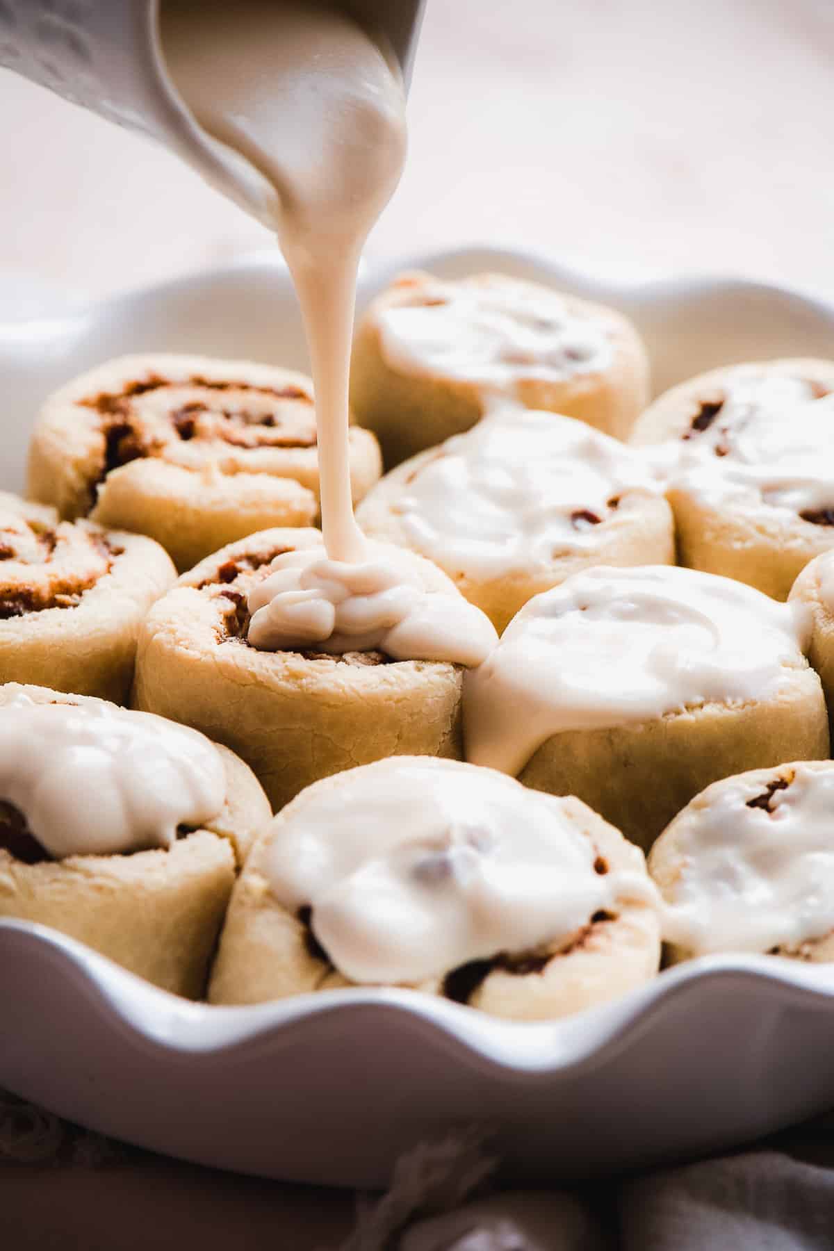 Icing being poured over top of baked cinnamon rolls.