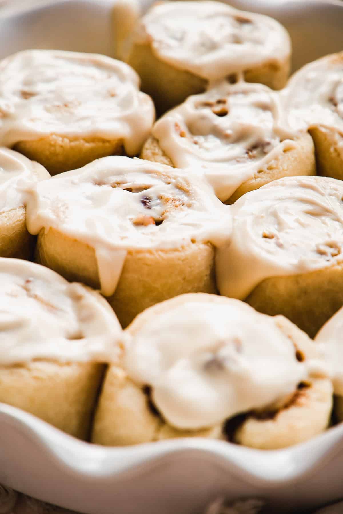 Up close view of baked cinnamon rolls with icing in a pan.