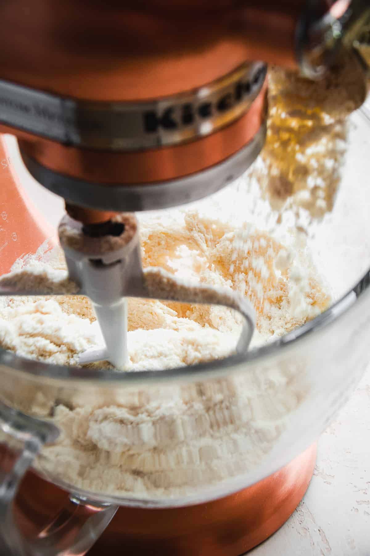 Mixer with flour being poured into the glass bowl.