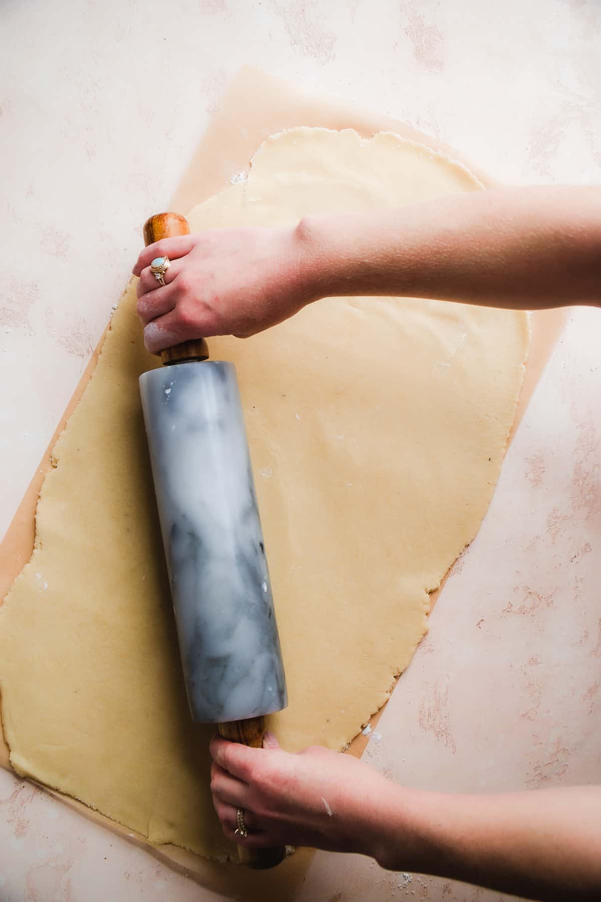 Hand rolling out cinnamon roll dough on parchment paper.