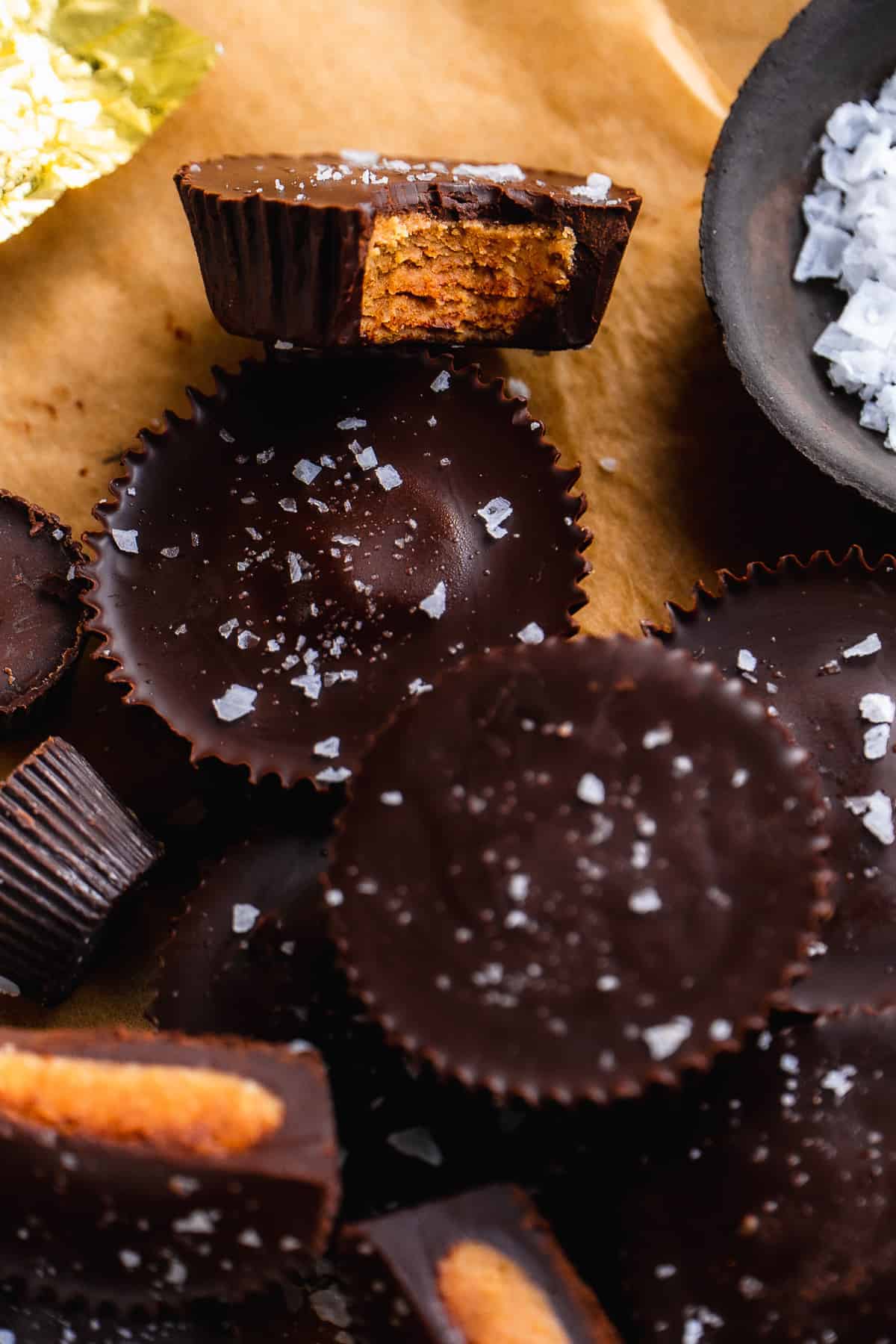 A peanut butter cup with a bite taken out of it on parchment paper with sea salt on top.