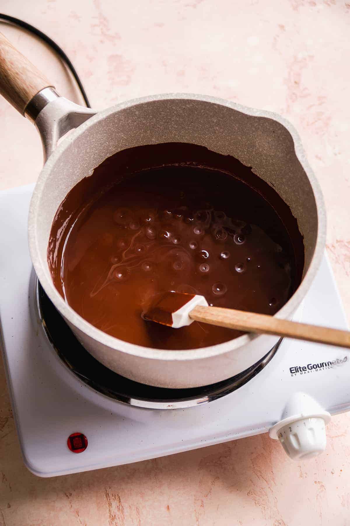 A gray pot with melted chocolate inside and a spatula resting on the edge.