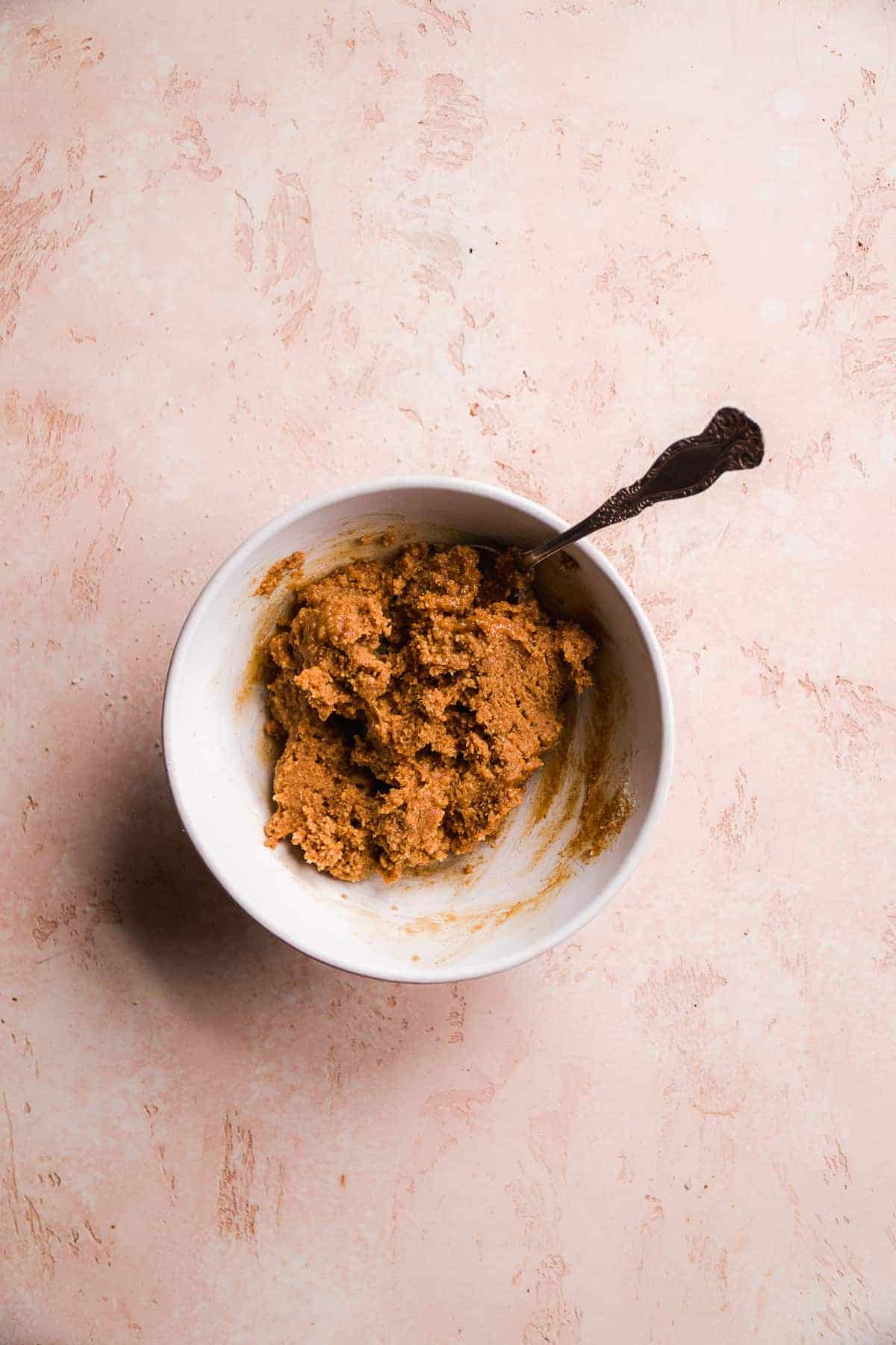 White bowl with thick peanut butter mixture inside and a spoon.