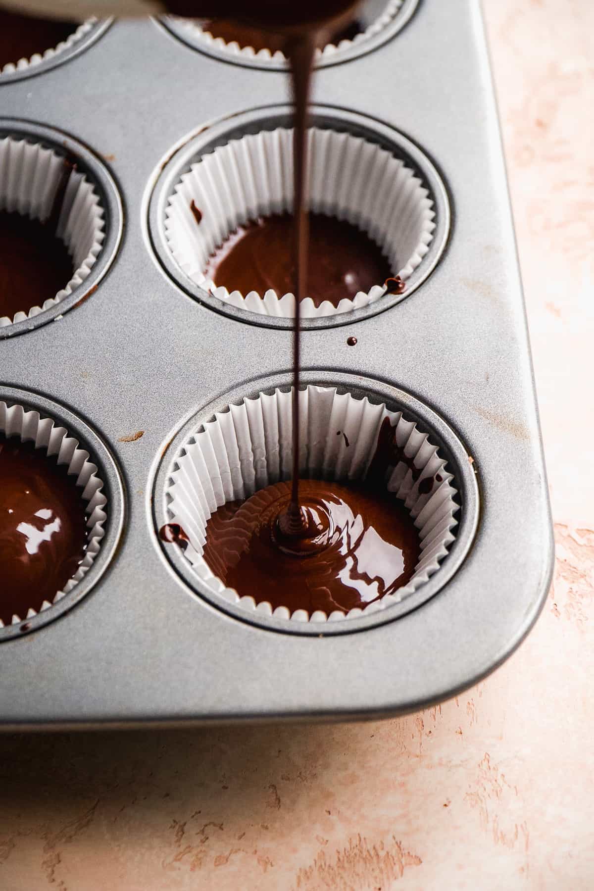 Chocolate being poured into a muffin pan with liners.