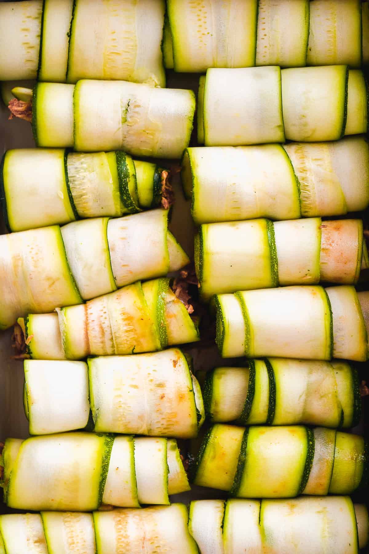 Overhead view of zucchini roll ups with chicken inside lined up in a row.