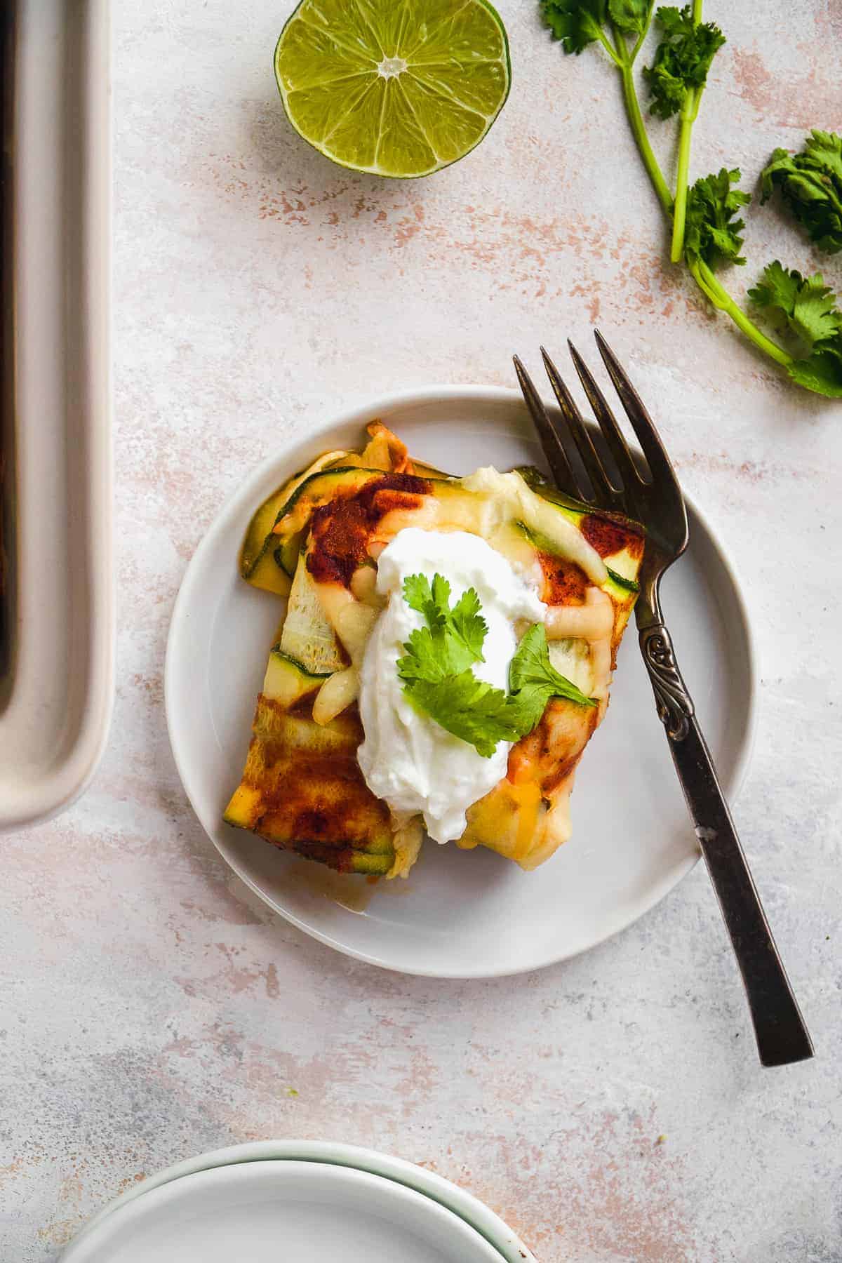 Overhead view of zucchini enchiladas on a white plate with a fork resting on the plate.