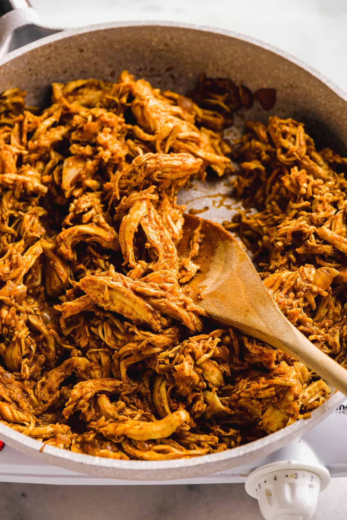 Skillet with pulled spiced chicken and a wooden spoon.