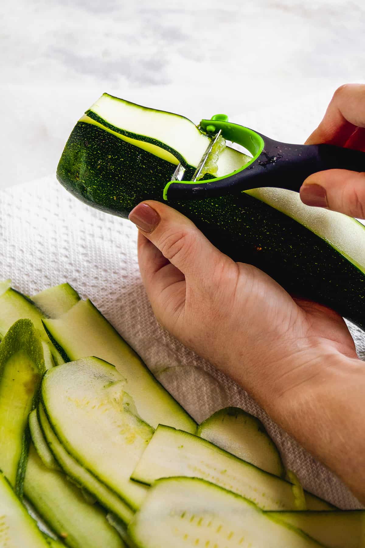 Hand peeling zucchini into thin strips.