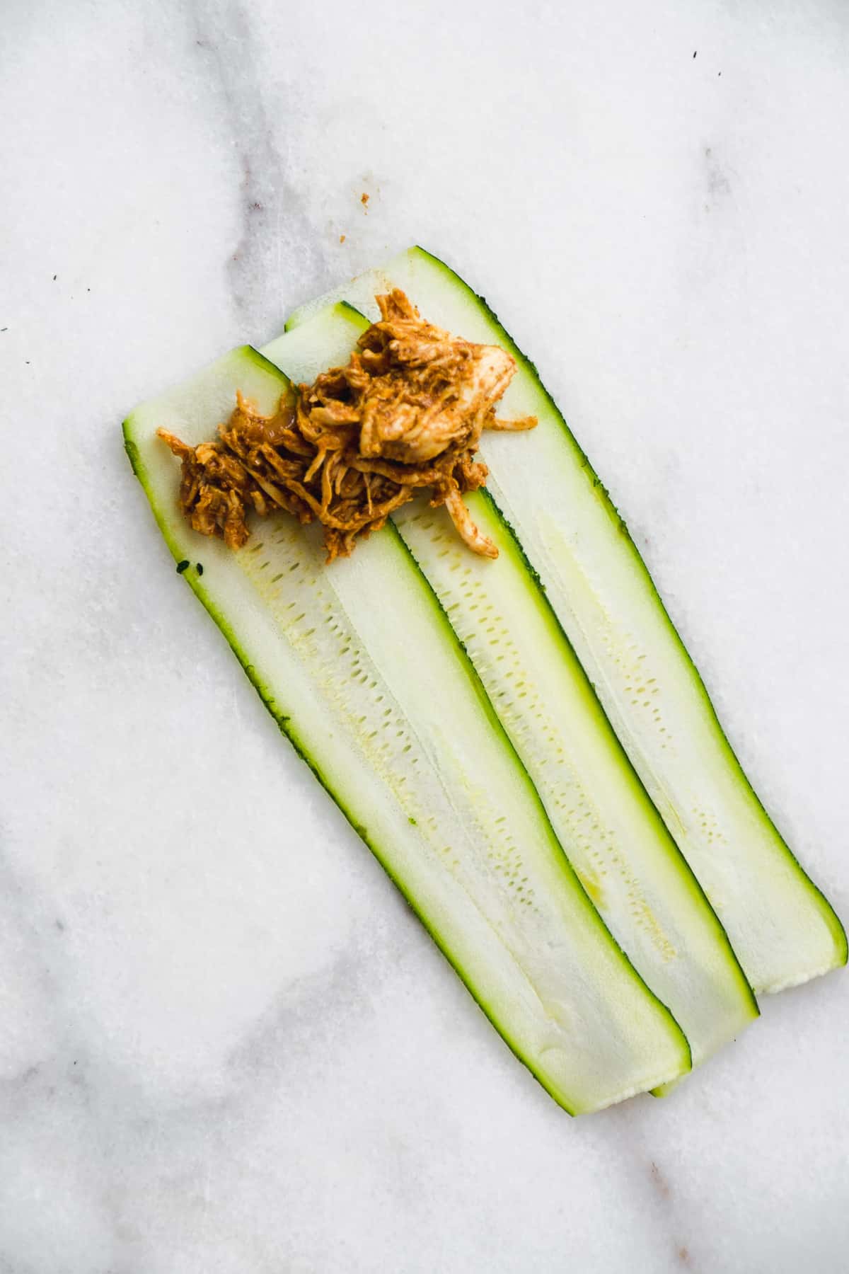 Zucchini strips with pulled chicken about to be rolled up.