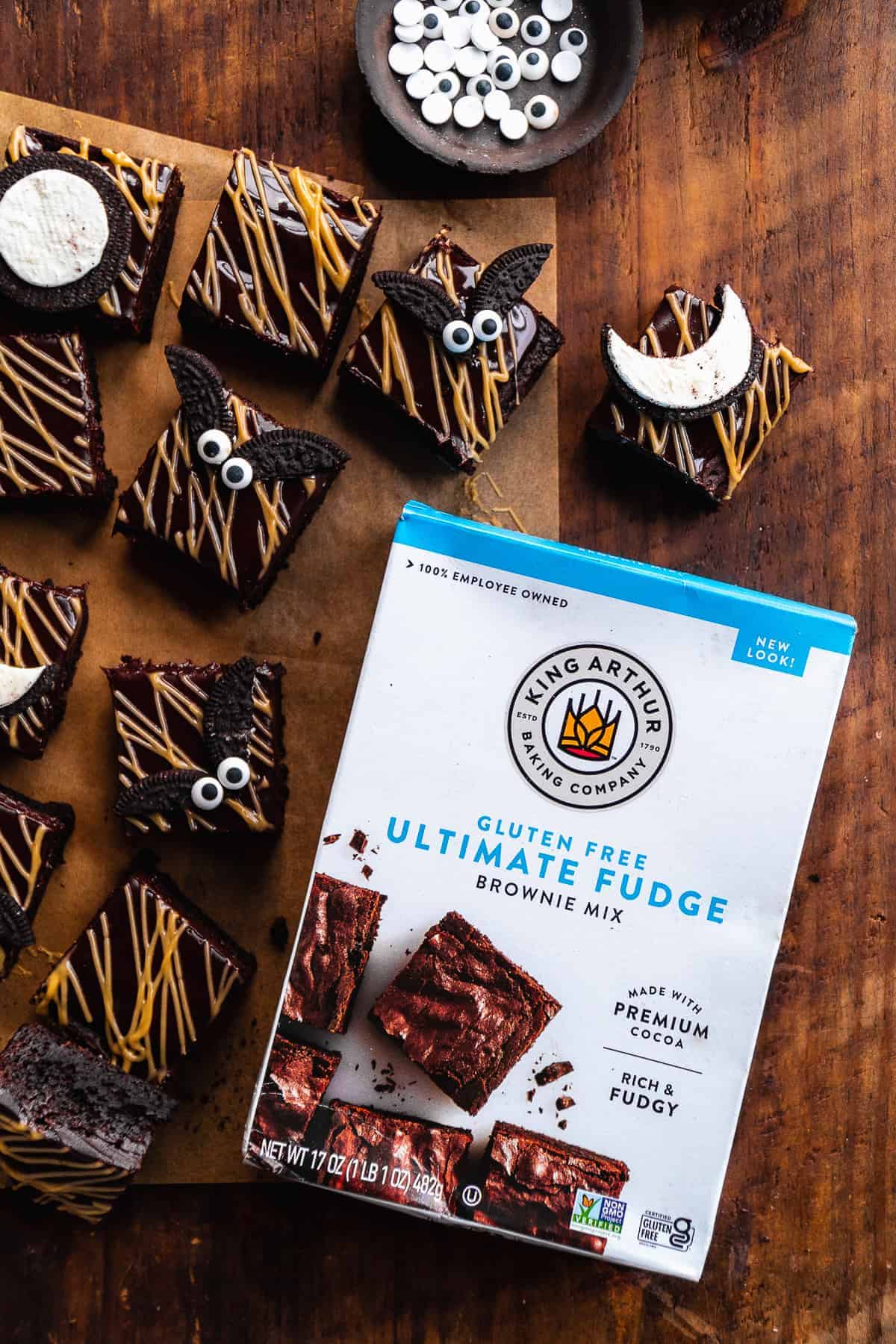 Overhead view of a white box of brownies on a wooden surface with brownies scattered around.