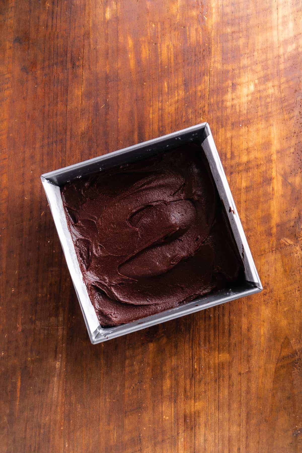 Square brownie pan with brownie batter inside about to be baked.