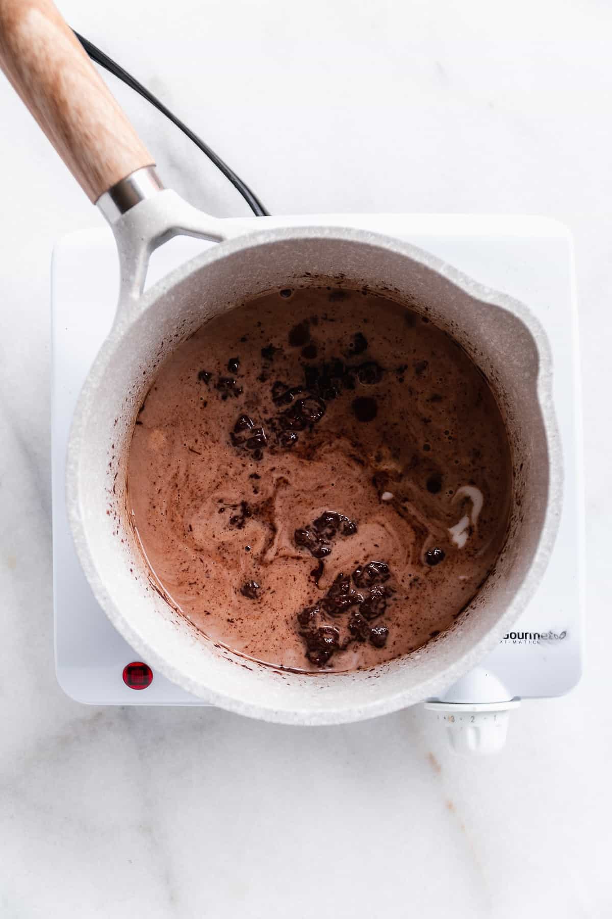 A gray pot on a burner on marble surface with chocolate mixture inside.