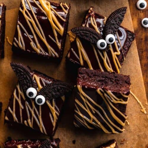 Overhead view of brownies with peanut butter drizzle on top and oreo bats on parchment paper.