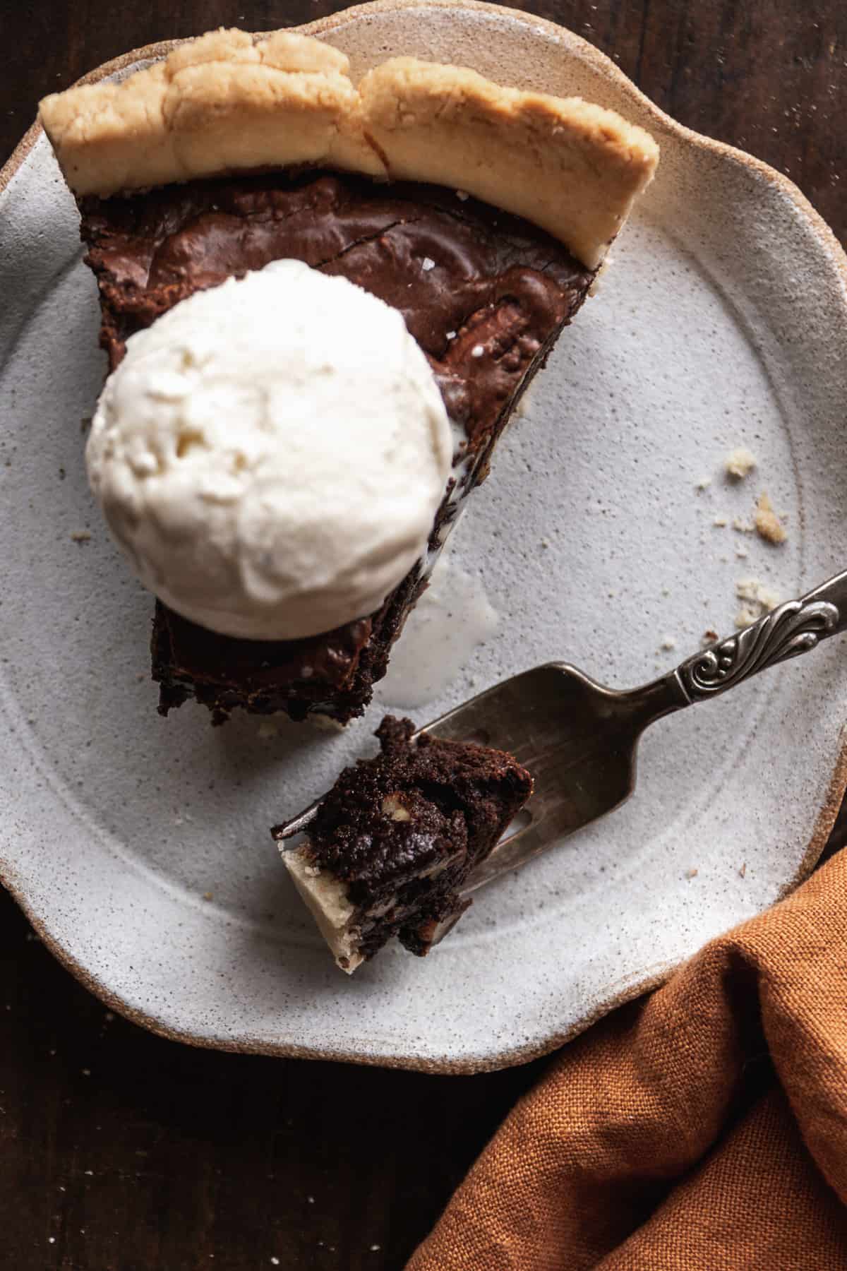 A slice of brownie pie with ice cream on top and a fork on the side.