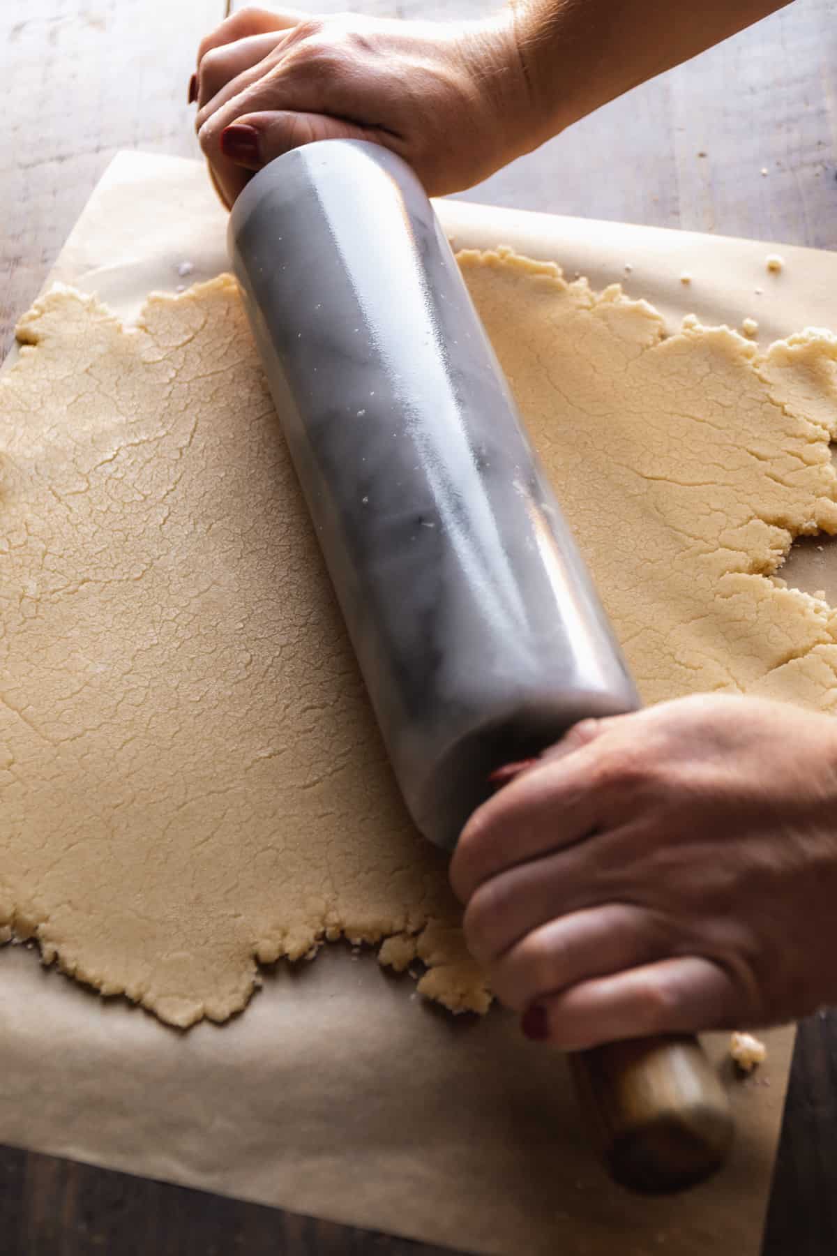 Person rolling out gluten free pie dough on parchment paper.