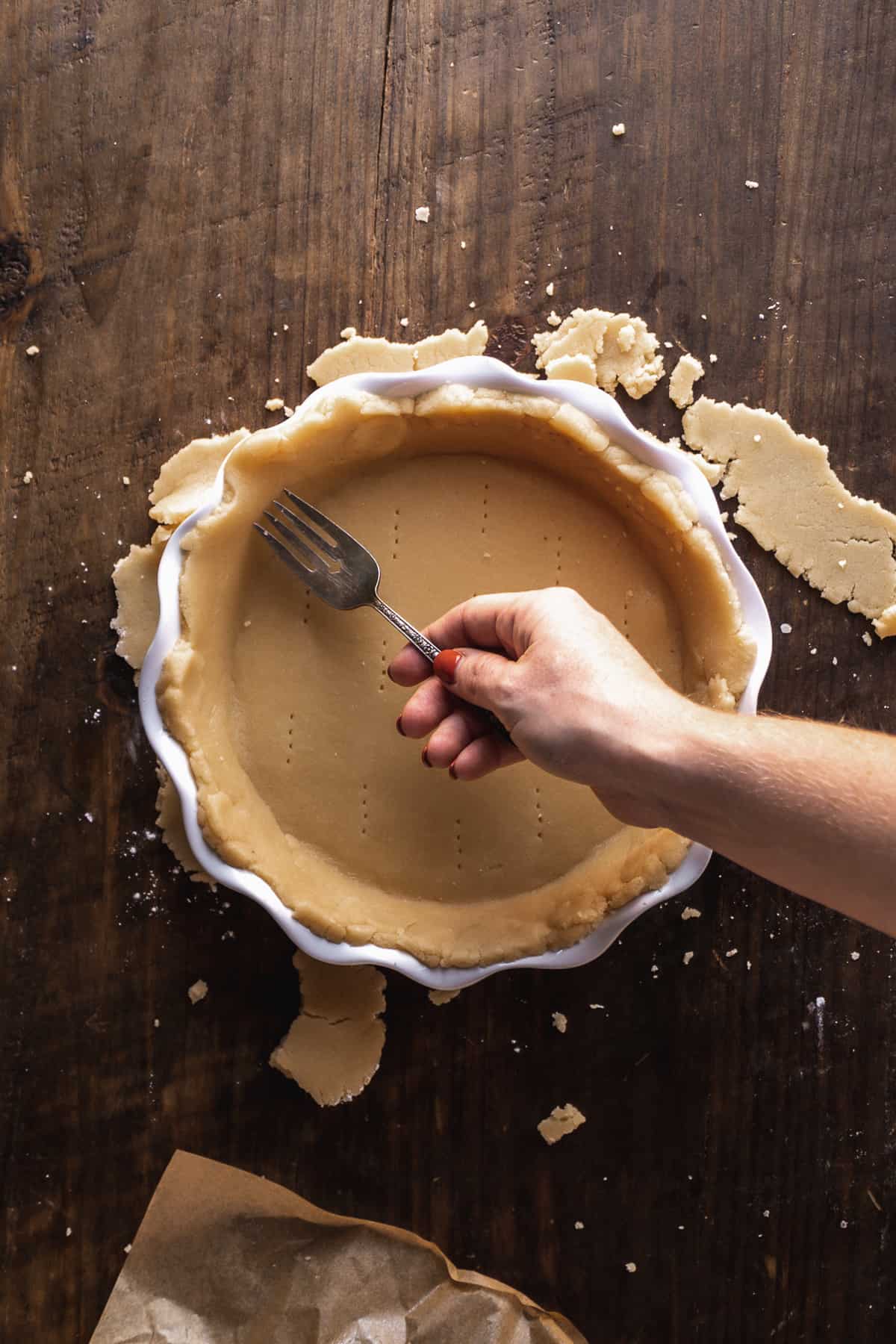Person poking holes in pie dough in a pie pan.