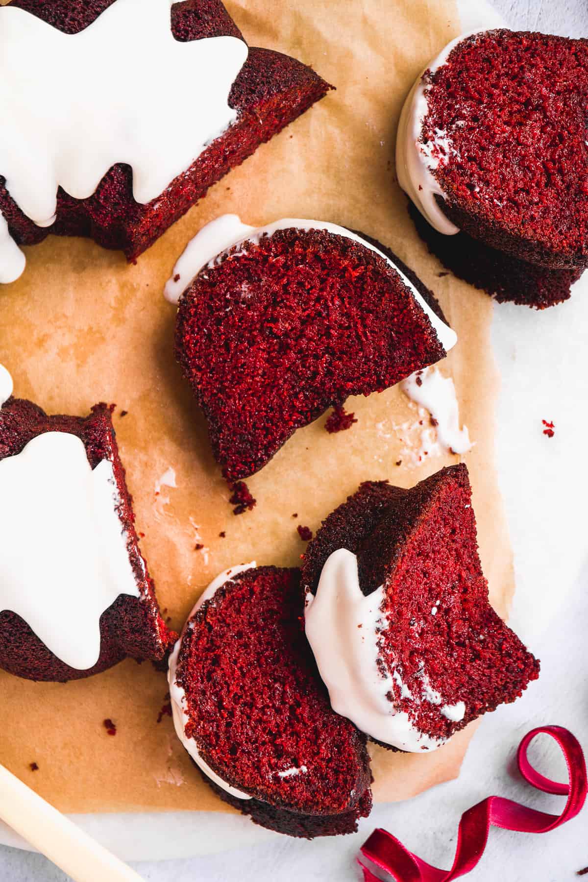 Red velvet bundt cake slices with icing scattered on parchment paper.
