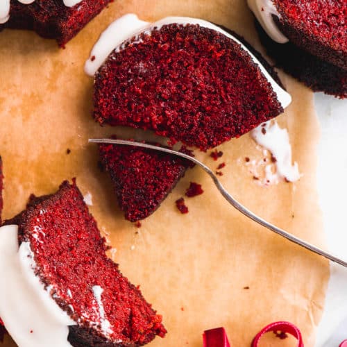 red velvet bundt cake scattered on parchment paper with a fork taking a bite out of a slice.