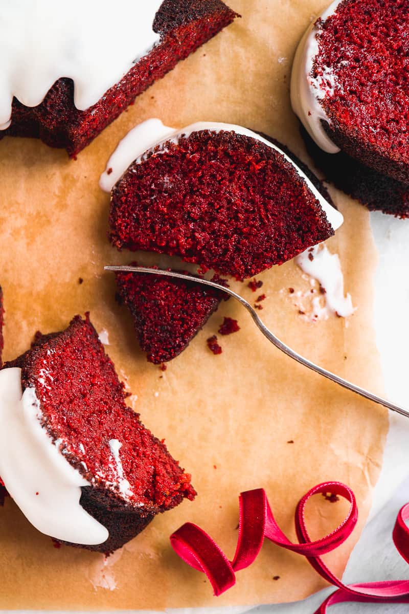 red velvet bundt cake scattered on parchment paper with a fork taking a bite out of a slice.