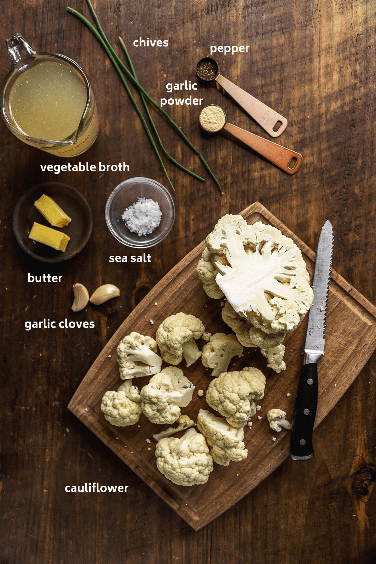 Cauliflower mash ingredients on a wooden surface with labels in white.