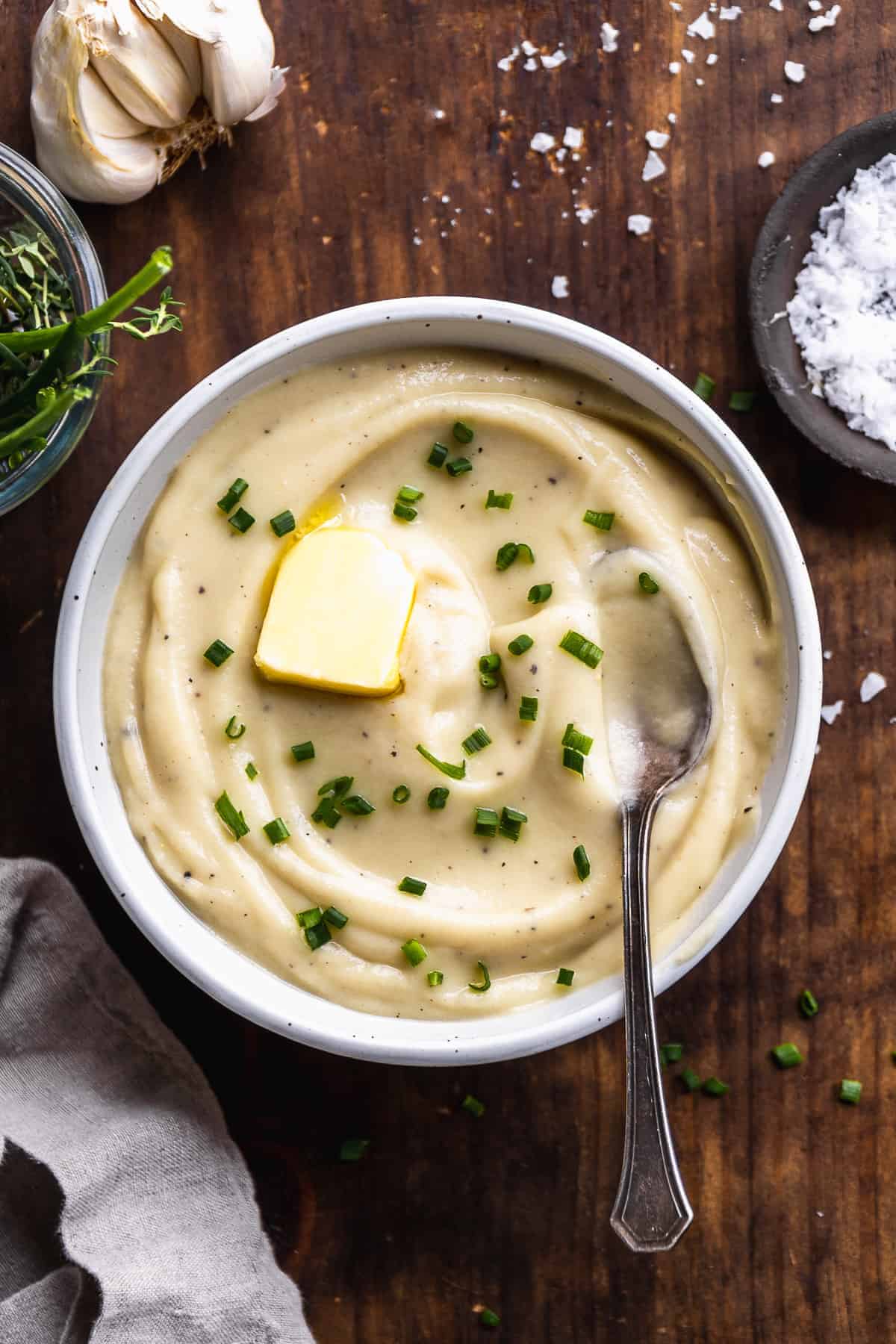 Bowl of mashed cauliflower with chives and butter on top and a spoon resting inside.