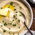 Up close view of a bowl of cauliflower mashed potatoes with a spoon inside.