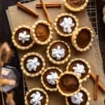 Mini dairy free pumpkin pies with whipped cream scattered on a cooling rack.