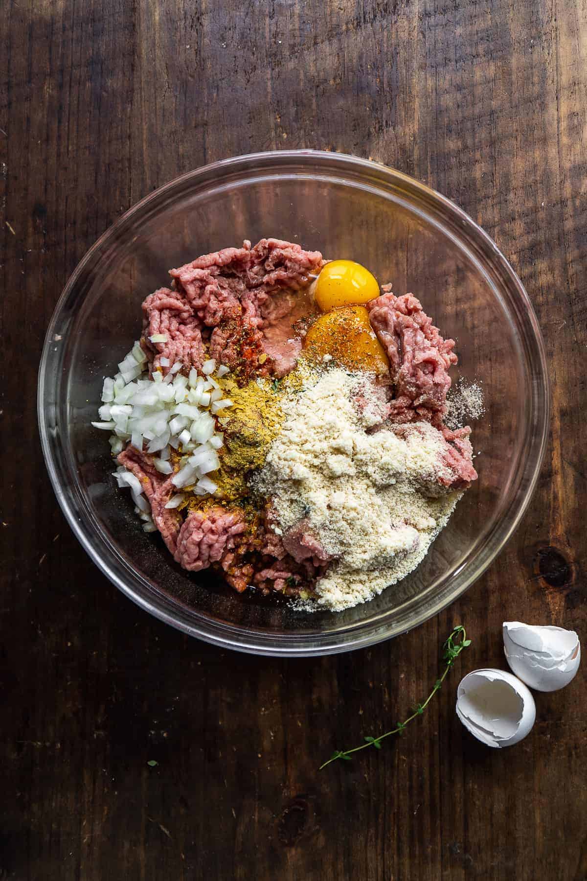 Turkey meatball ingredients in a glass bowl on a wooden surface.