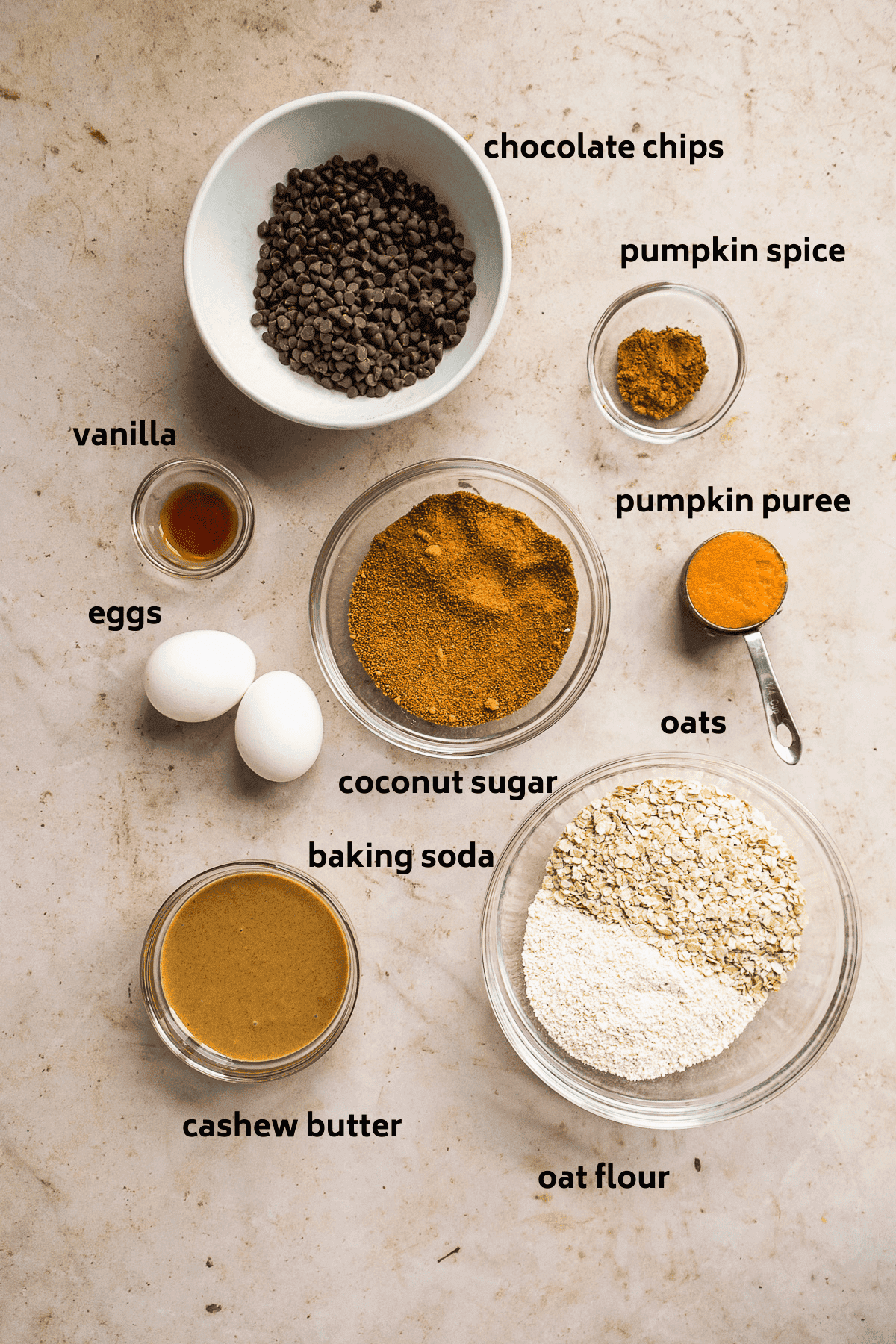 Overhead view of pumpkin cookie ingredients on a tan surface with labels in black.