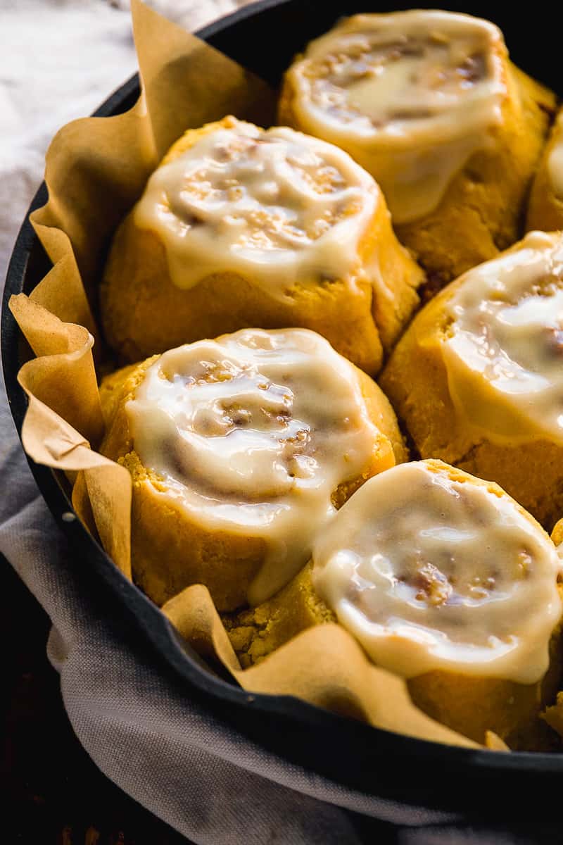 Pumpkin cinnamon rolls with icing in a black cast iron pan.