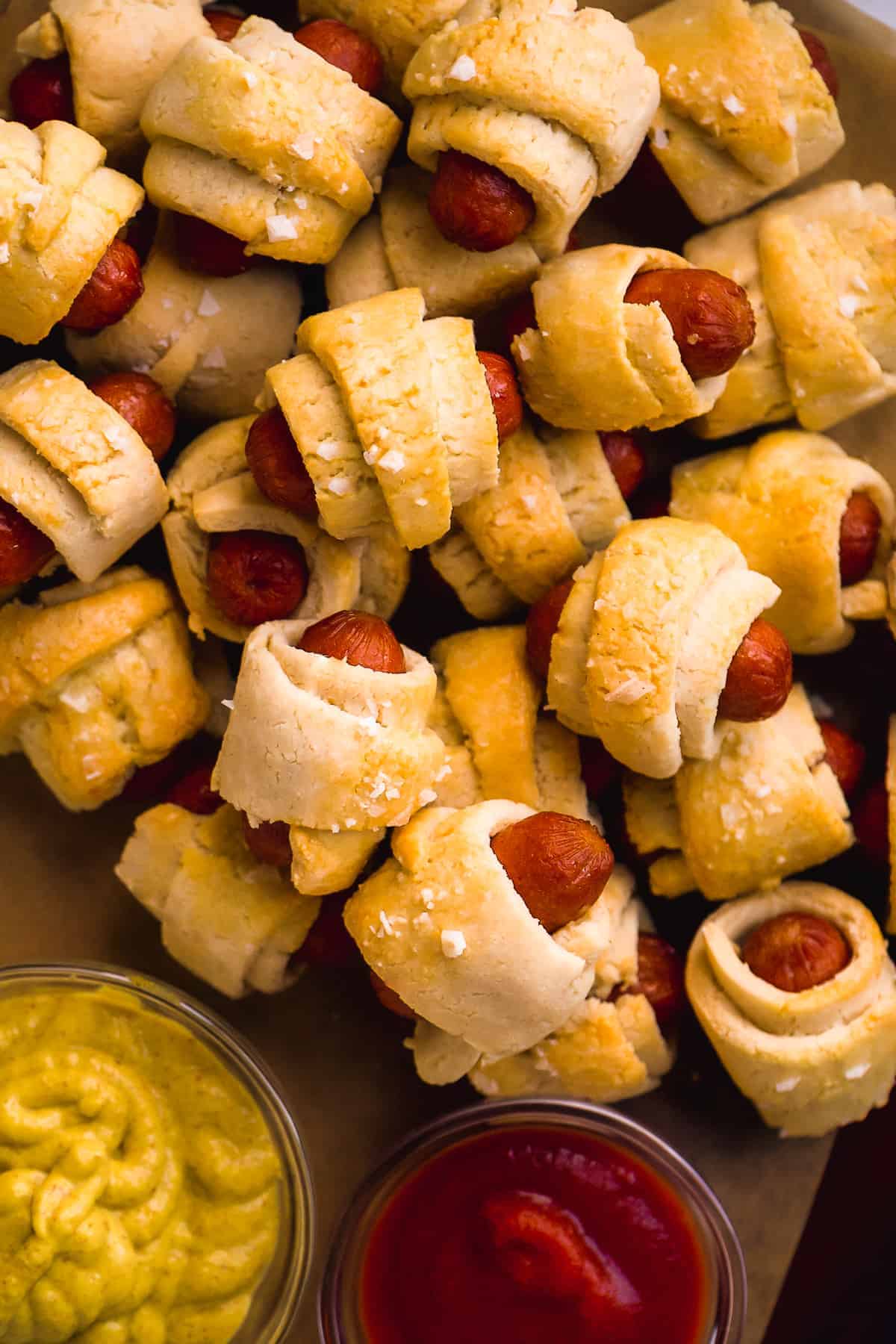 Overhead view of a pile of gluten free pigs in a blanket on a wooden platter.