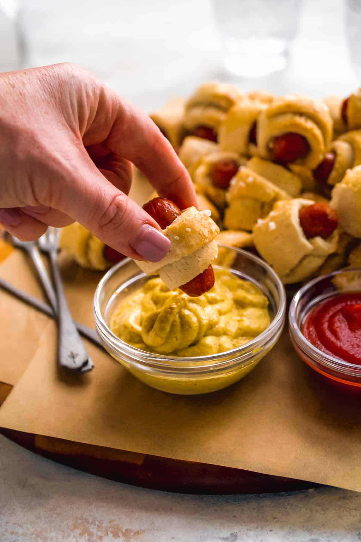 Person about to dip a pig in a blanket in mustard.