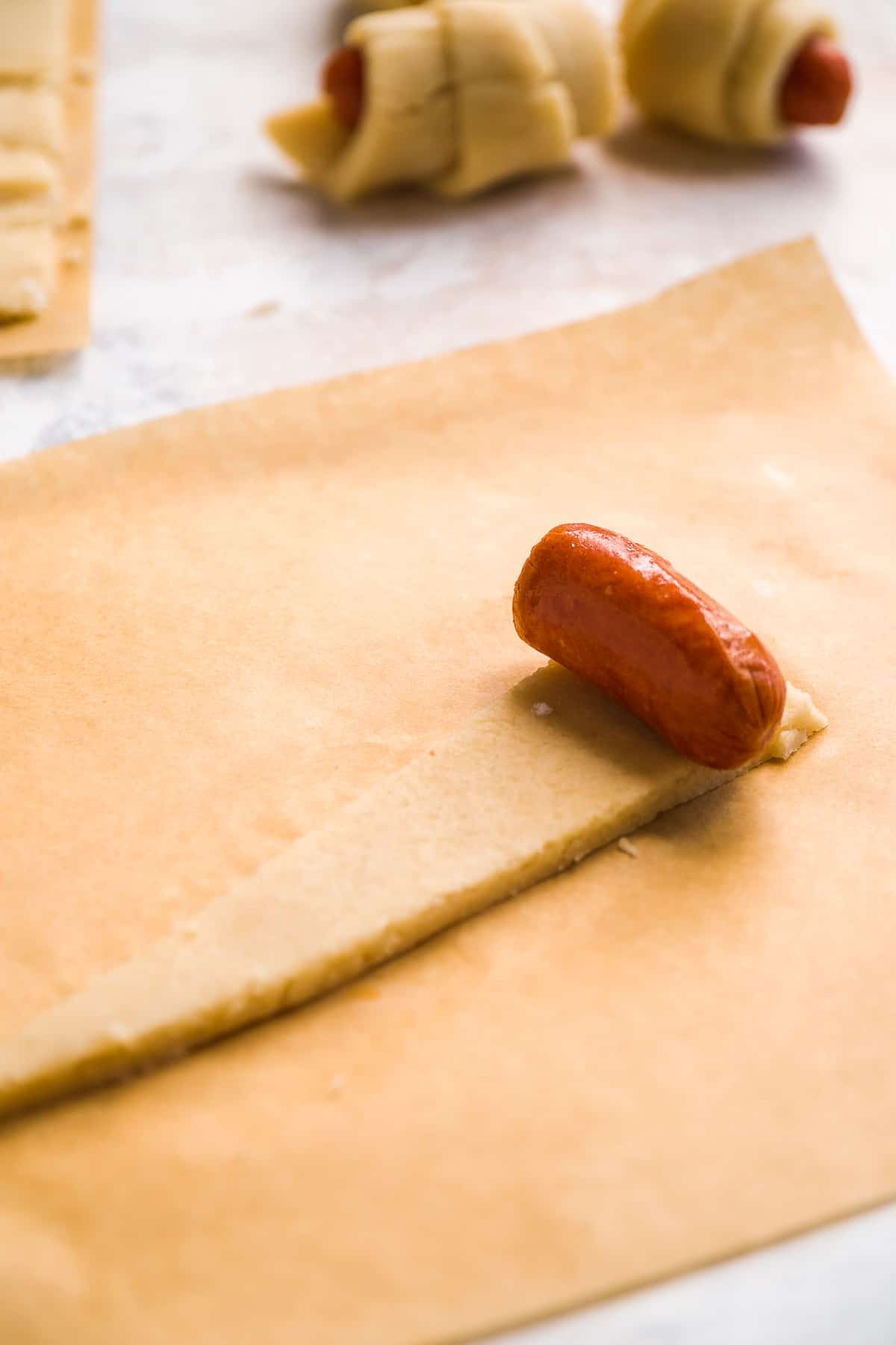 Triangular piece of dough with a sausage on top about to be rolled up.