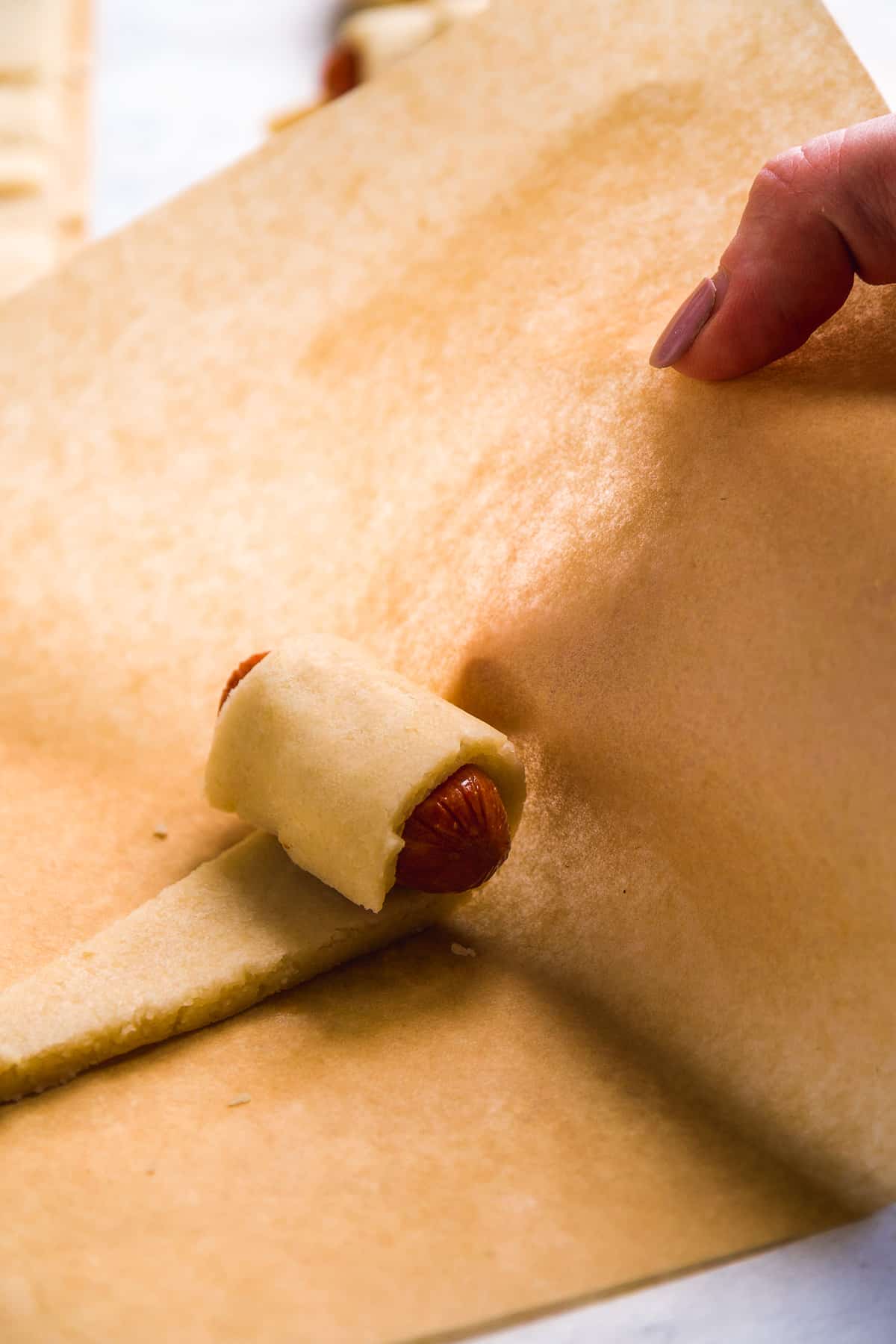 A mini sausage being rolled up in gluten free dough.