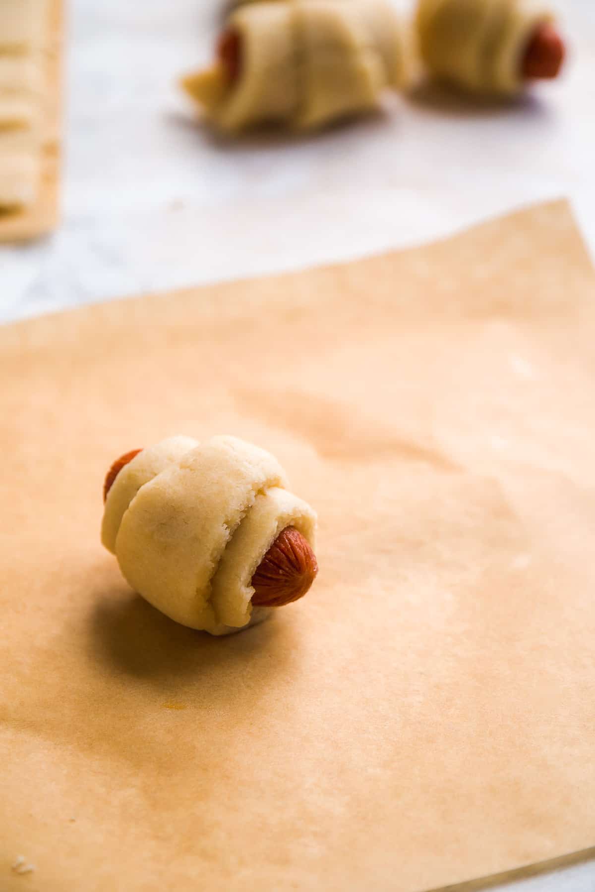 Unbaked pig in a blanket on brown parchment paper.