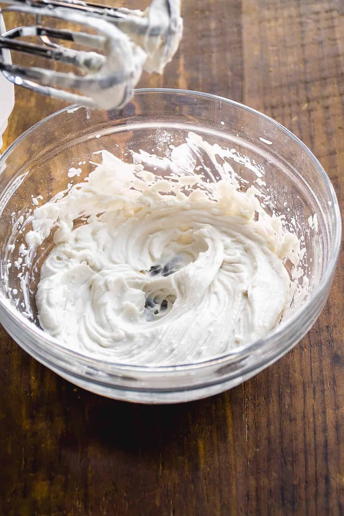 Glass bowl with whipped coconut cream and a mixer to the side.