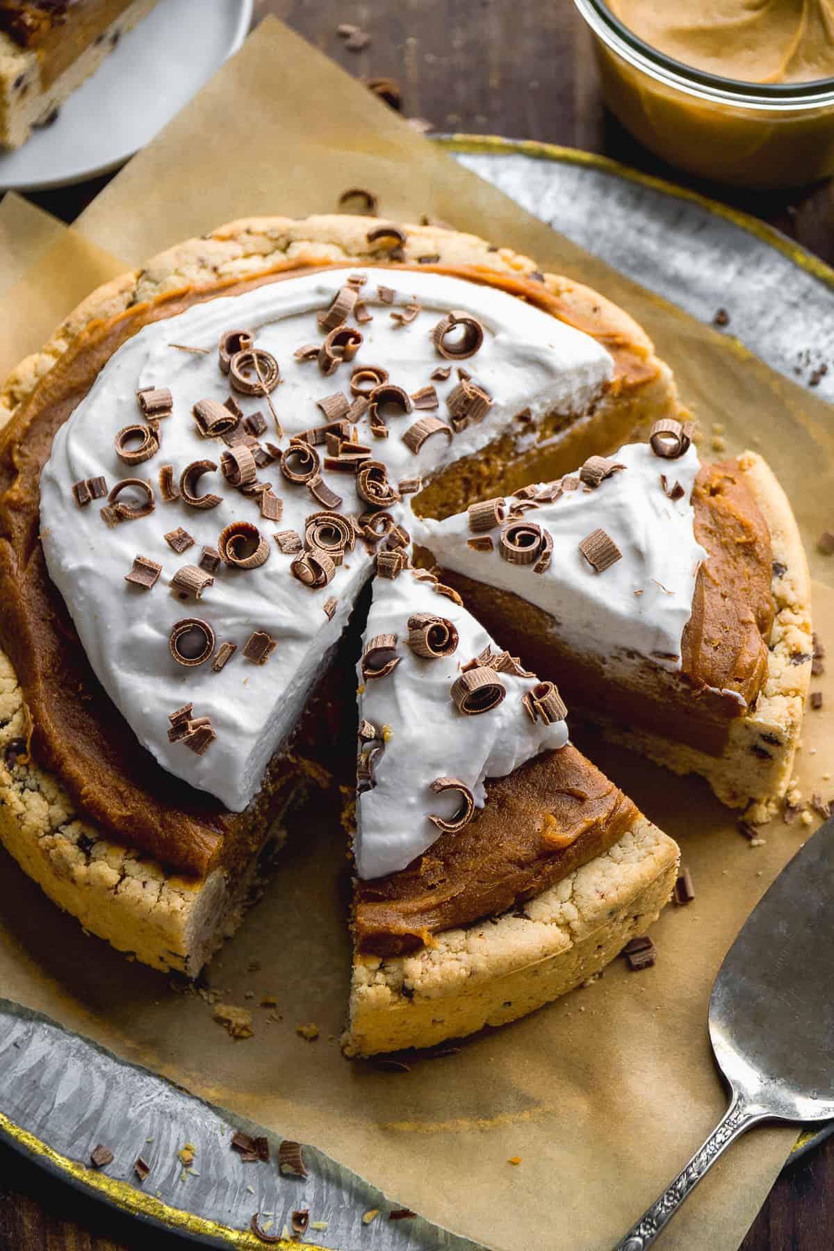 Vegan peanut butter pie with whipped cream on top on parchment paper with two slices cut out.