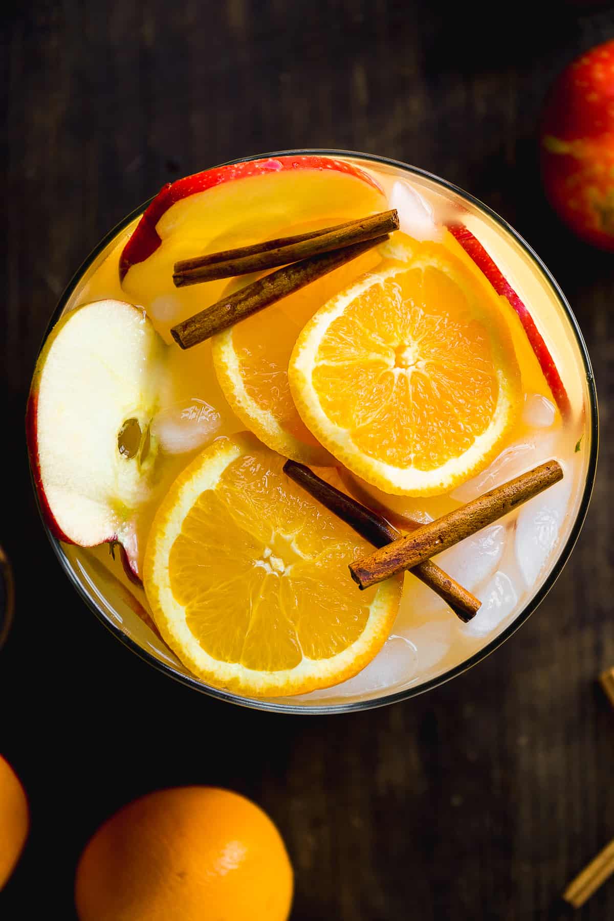 Overhead view of a pitcher with orange and apple slices and cinnamon sticks on top.