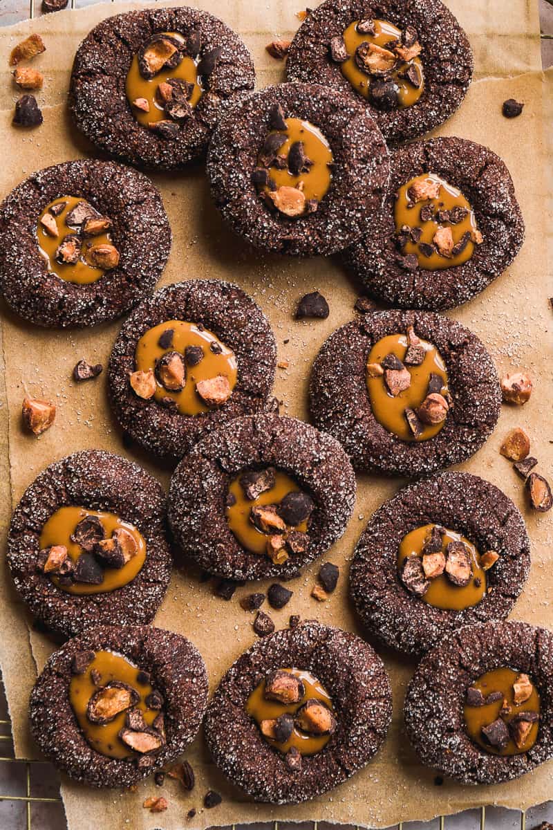 Chocolate gluten free thumbprint cookies scattered on brown parchment paper.