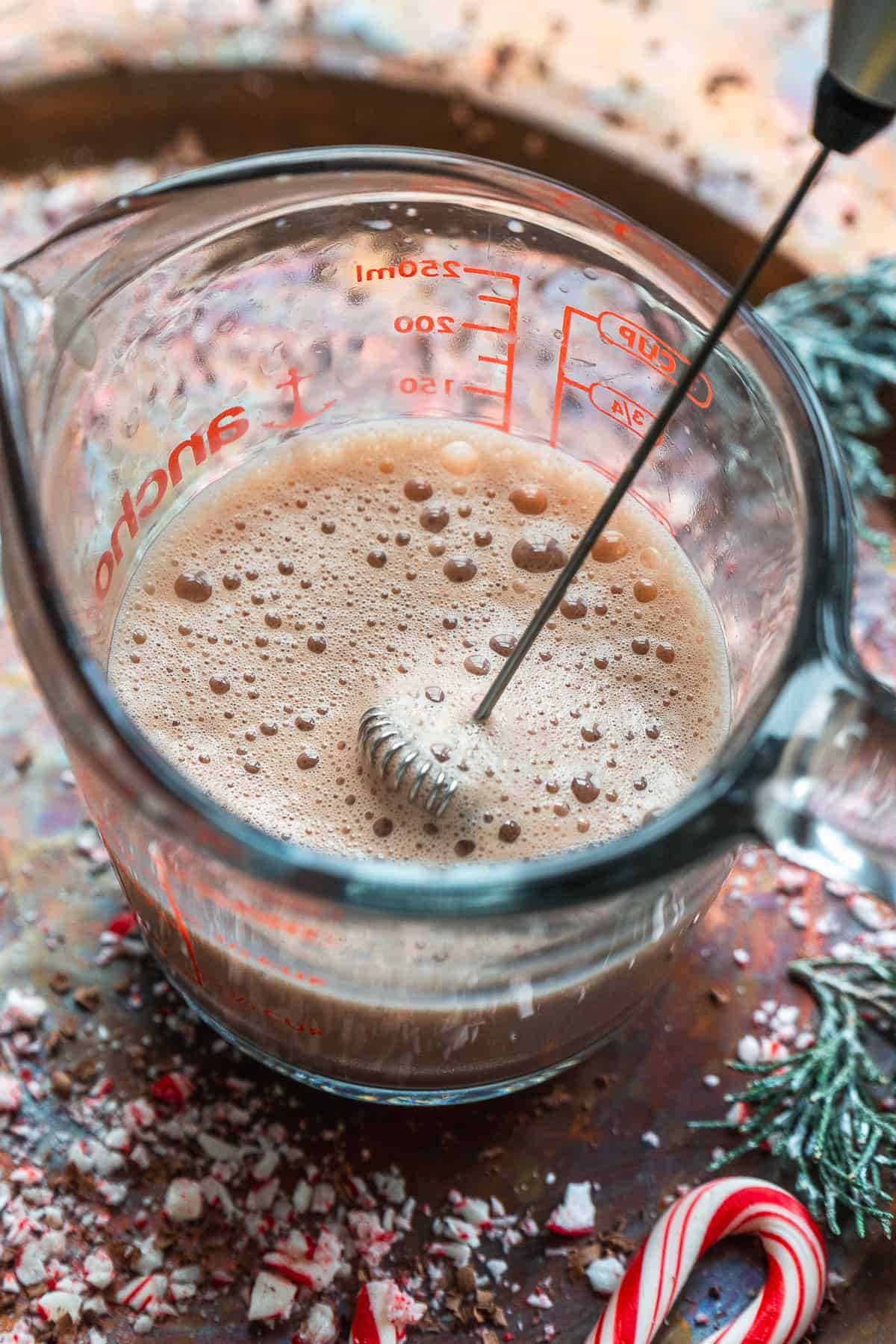 Chocolate creamer being frothed in a glass.