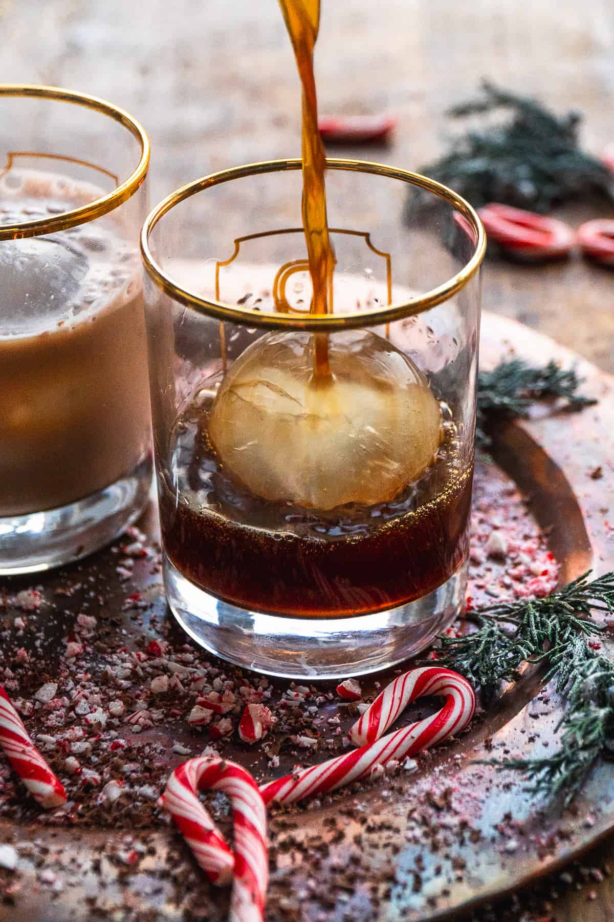 Boozy coffee being poured into a cocktail glass with a circular ice cube.