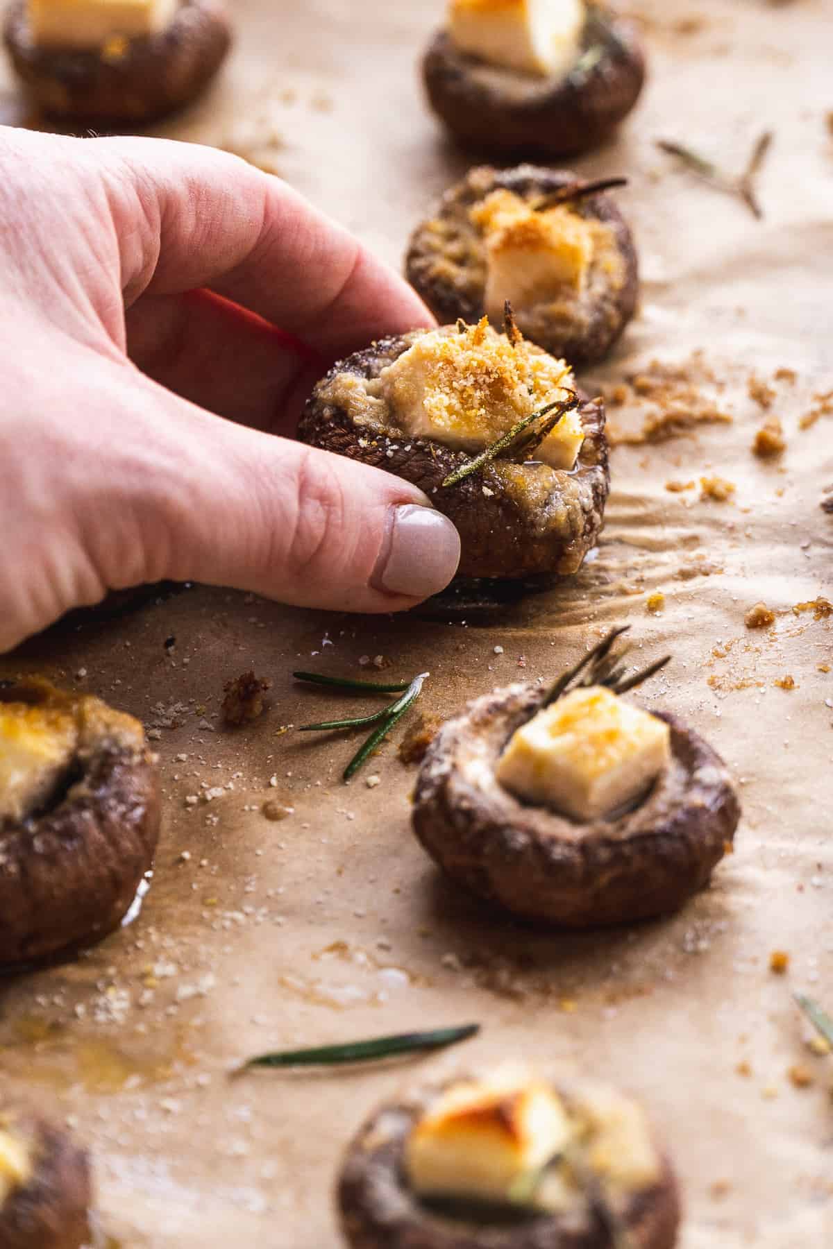 Person grabbing a stuffed mushroom off a baking sheet.