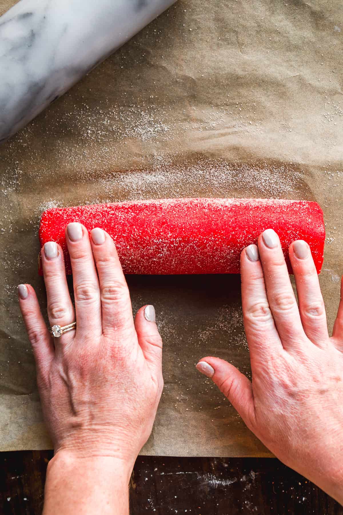 Person rolling red cookie dough log in sugar.