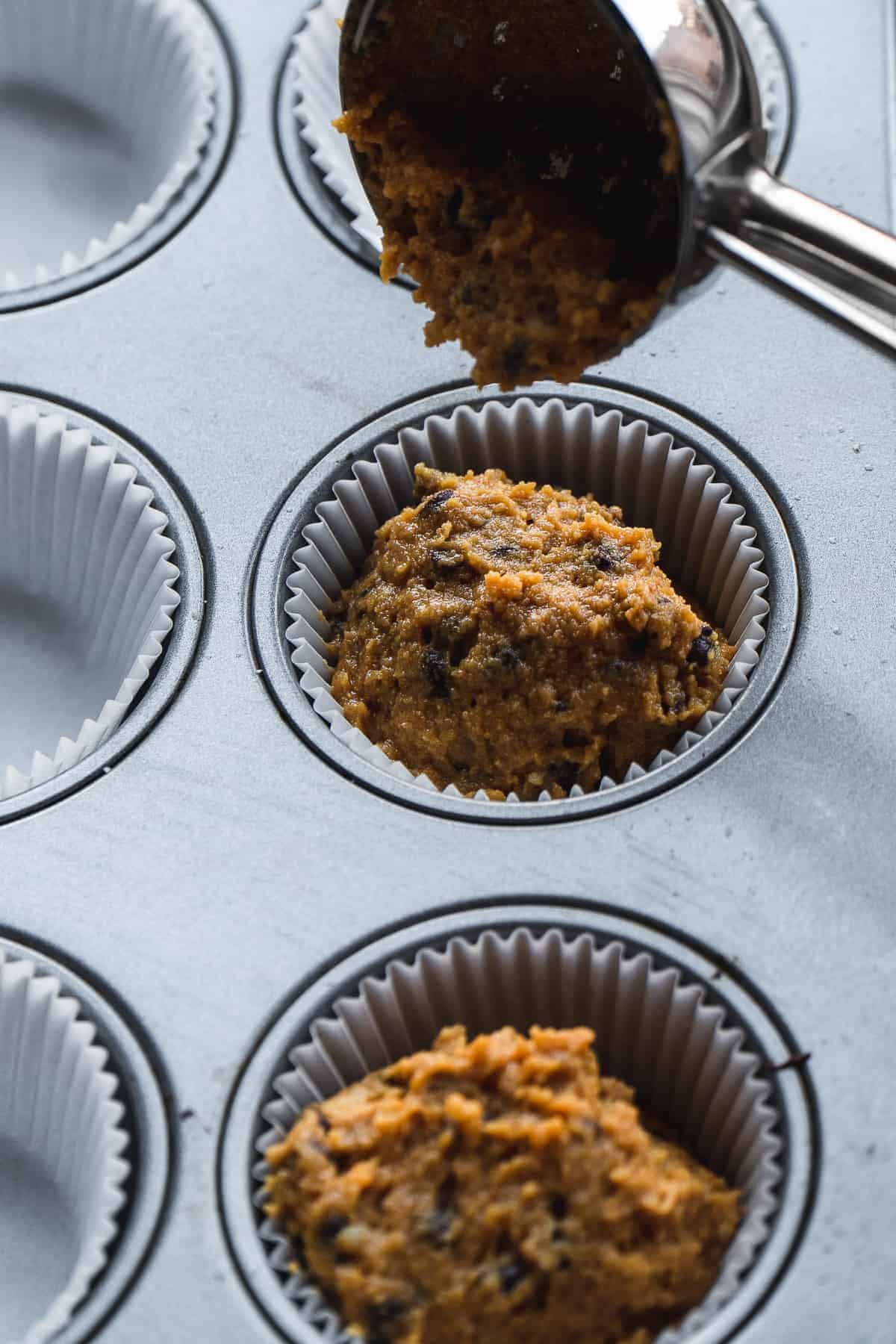 Muffin batter being scooped into muffin liners.