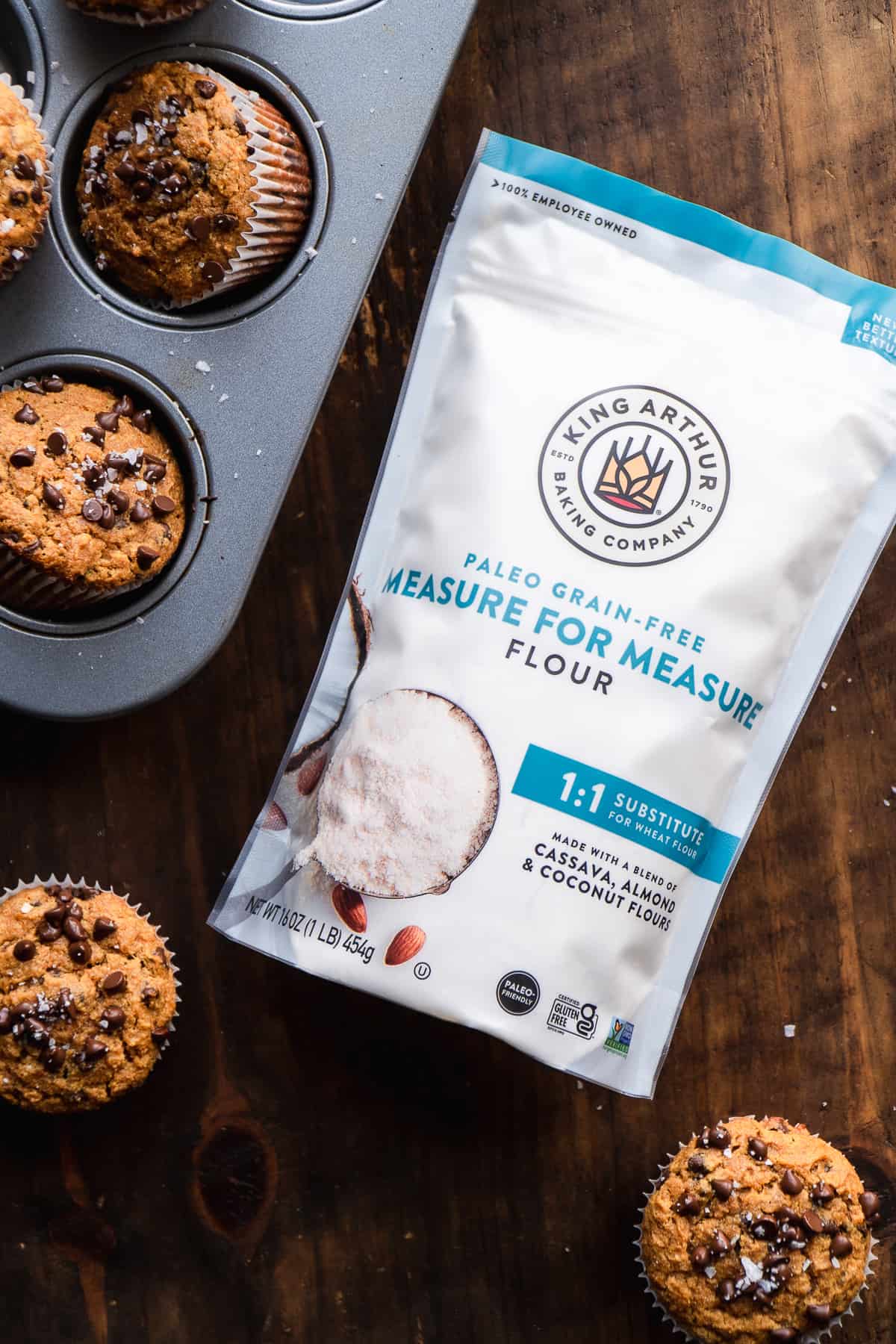 A bag of paleo flour on a wooden surface with muffins on the side.