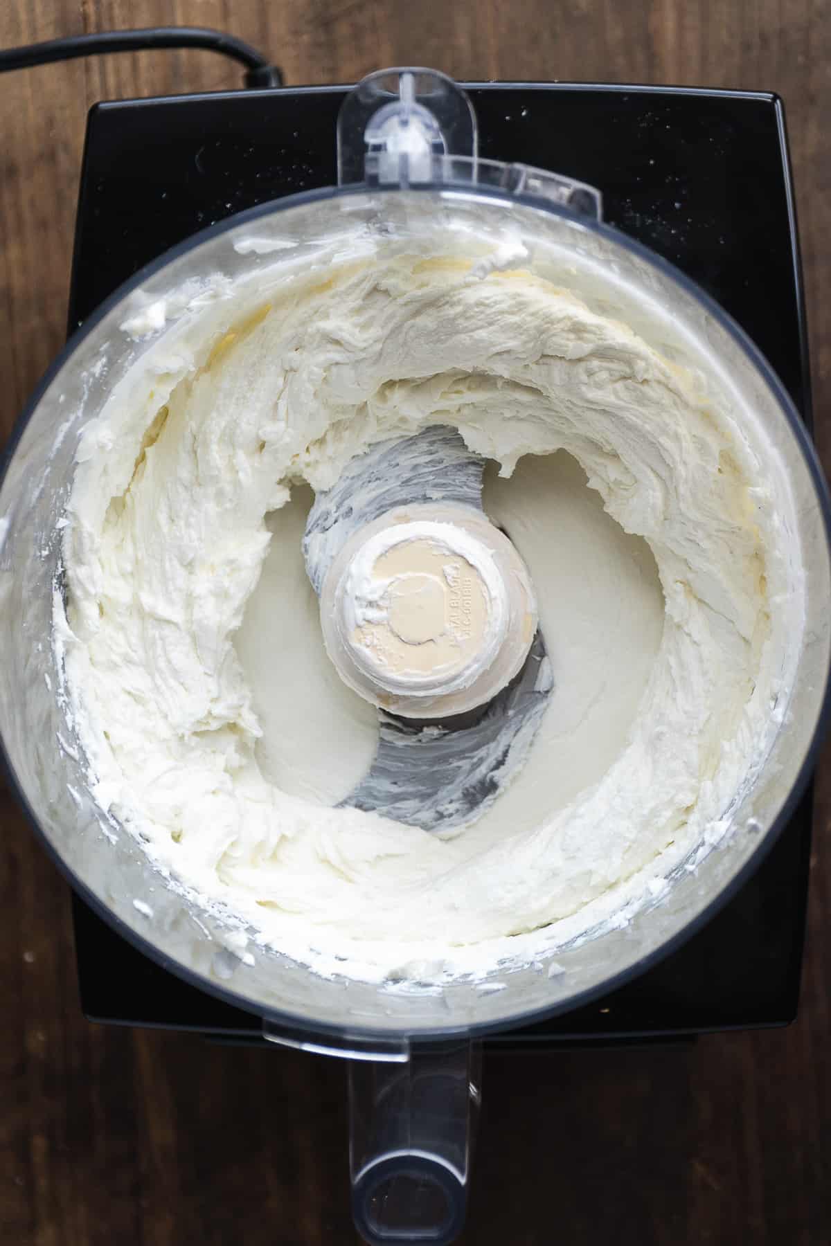 Overhead view of a food processor with whipped goat cheese and greek yogurt.