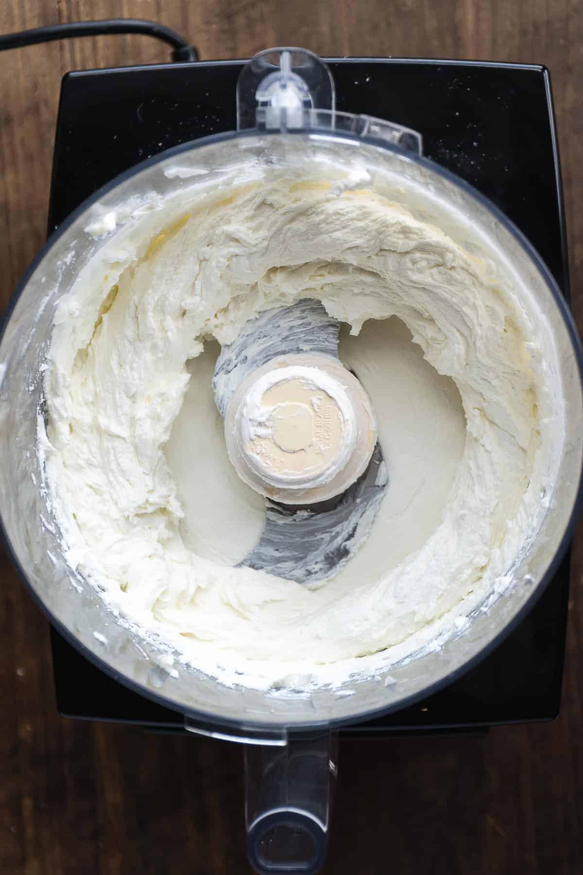 Overhead view of a food processor with whipped goat cheese and greek yogurt.