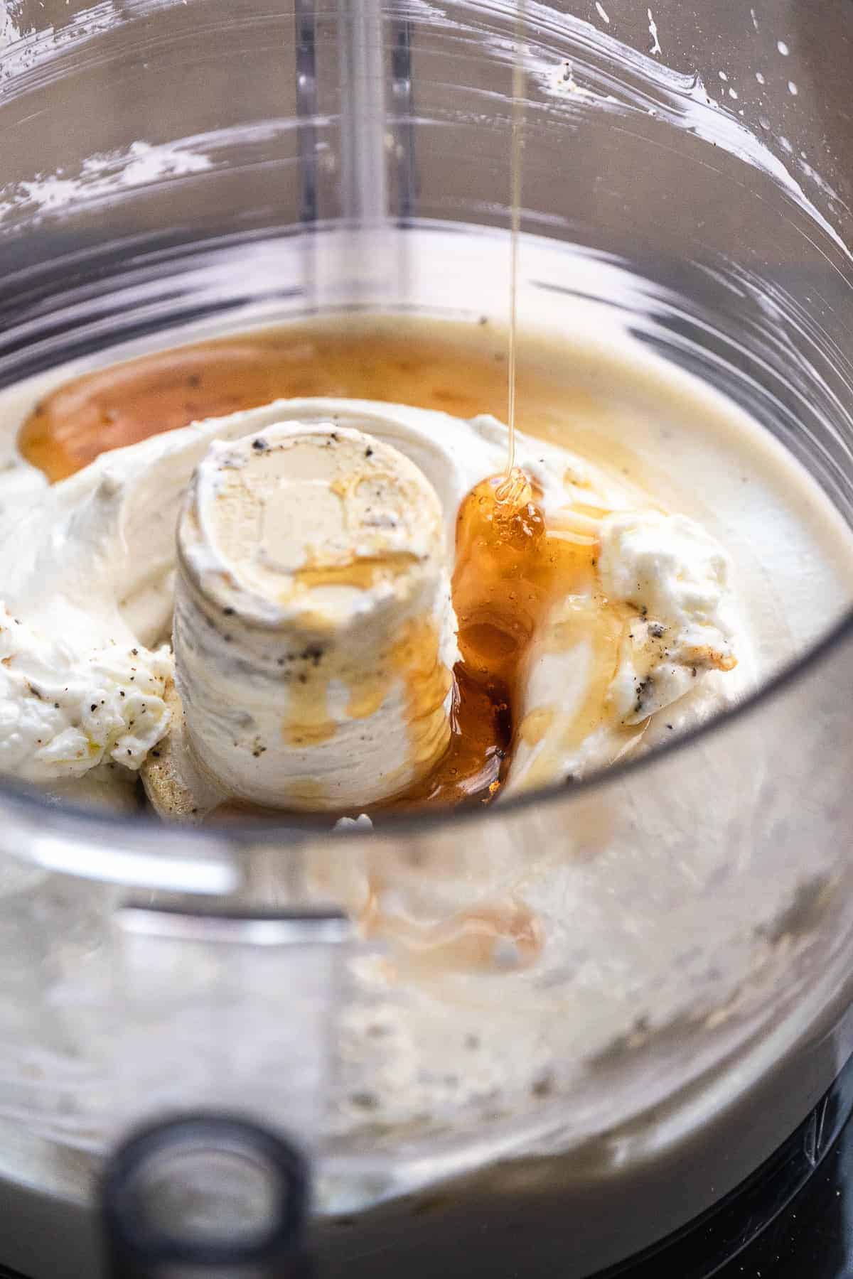 Honey being drizzled into a mixer with whipped goat cheese.